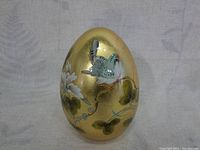 Large goldleaf egg with blue bird and green leaves design on one side