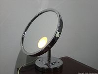 Front view displaying circular lighted mirror on round base with power cord