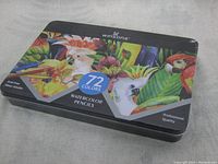 Sealed metal tin case with colorful bird and floral artwork, showing product name, brand, and number of colors.