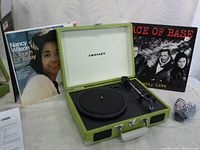 Open lime green Crossley turntable with tonearm and control knobs, showing white interior lid with brand name, paired with two vinyl records.