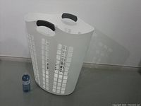 Image showing large white laundry basket standing on floor next to a water bottle for size reference.
