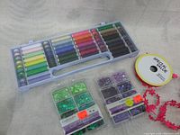 Plastic container with multicolored bobbins wound with new thread, and two small boxes of assorted sequins in green and purple, plus a spool of pink floral trim ribbon.