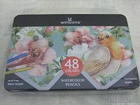 Sealed metal tin box of Winsons watercolor pencils showing the front with floral and bird illustration, '48 colors', and product branding.