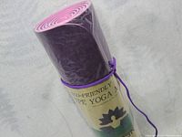 Yoga mat rolled up vertically showing the eco-friendly label and lotus flower logo, purple color.