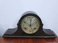 Front view of Sessions mantel clock showing the arched wooden case and glass-covered clock face with Arabic numerals.