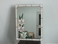Front view of rectangular stained glass mirror with white and pink flower pattern on the left bottom corner and white glass border.