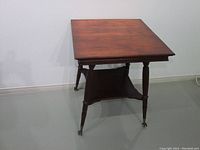 Full view of Victorian mahogany square table showing two-tier design and brass claw casters on legs.