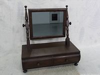 Front view of dark stained walnut dresser mirror with rectangular adjustable mirror and two drawers with wooden knobs, on small round feet.