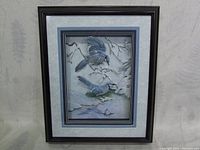 Front view of framed 3D paper tole art showing two Blue Jays in a winter scene under glass with dark wooden frame.