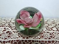 Front angle view showing the pink flower inside clear glass paperweight resting on lace.