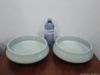 Two wide, shallow, grey glazed pottery bowls side by side with water bottle for scale