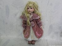 Full view of vintage porcelain doll standing with pink coat and white dress visible