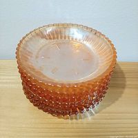Stacked view of seven peach carnival glass candy dishes showing hobnail texture and iridescent finish.