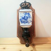 Front view of the porcelain wall mounted coffee grinder showing the blue floral decoration and wooden mount.