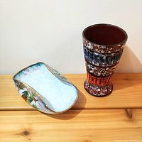 Overview photo showing the irregular-shaped bowl with painted pine cones and the tall speckled vase side by side