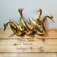 Front view of brass swans wall decor showing four swans sculpted together, shiny but with some age-related wear.