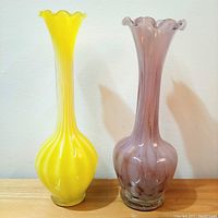 Two slender tulip-shaped glass vases, one yellow with white candy stripes and one amethyst with white marbling, shown side by side