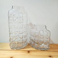 Front and side view of two clear glass vases with dimpled square textured bodies, one tall and narrow, one short and wide with oval opening.