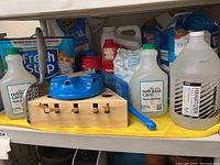 Overall view of cat care supplies collection including litter bags, pee pads, hand sanitizers, scoops, and wooden cat scratcher toy on yellow surface