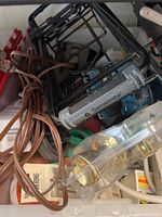 Close-up photo showing black metal cart frame with wheels, Samsonite item, and brown electrical cords tangled together with additional small hardware.