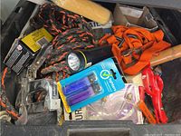 Overview of mixed tools including staple gun, rope, flashlight, lighter refills, red pliers, orange straps, box of screws and nails, wooden handled tool.