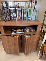 Wooden cabinet containing various VHS and DVD movies on shelves and inside closed compartments.
