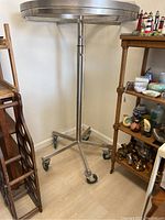 Full view of one round metal clothing rack showing the 5 caster wheels and round top ring, placed on wood floor.
