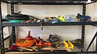 Two shelves showing coiled hoses, various hand tools, circular saw, extension cord and oil can.