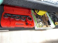 Red plastic case and adjacent cardboard box filled with various hand tools and hardware