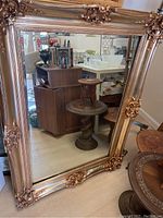 Full view of large gilded beveled mirror with reflected background showing detailed ornate frame and overall size.