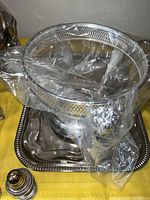 Photo showing the Corning coffee and tea warmer carafe with silver plated handle and exterior over clear glass, along with other silver plated items covered in plastic wrap.