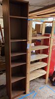 Front view of two shelving units, brown narrow particle board shelf and natural solid wood shelf