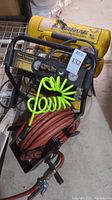 Overall photo showing yellow Campbell Hausfeld air compressor with black control panel, coiled green hose, brown hose on reel, and attached components.