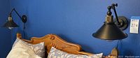 Pair of black metal wall sconces mounted on a blue wall over a wooden bed with pillows, showing scale and installation style.