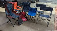 Seven assorted camp chairs and foam cushions arranged outside near trucks and pavement.