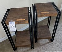 Two compact nightstands side by side showing overall design and size. Black metal frame with imitation wood top and lower shelf.