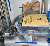 Plastic bins stacked containing various firearm accessories including cleaning supplies and manuals.