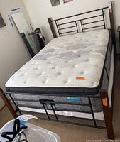 Full view of bed with mattress and box springs showing dark wood posts and black wrought iron metal headboard and footboard with mattress on top.