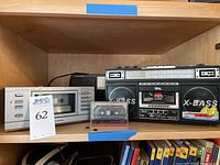 Wide shelf display of the Realistic cassette player on left, QFX X-Bass cassette recorder on right, and Roger Whittaker cassette in center front.