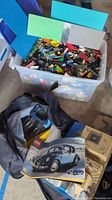 Open large plastic bin showing assorted loose LEGO bricks and several large baseplates (blue, green, grey)