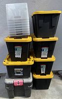 Stack of black storage tubs with yellow lids and several clear plastic open tubs on top, showing the lot of storage containers.