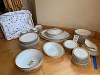 Photo showing full lot arranged on floor, including plates, cups, saucers, bowls, platters, and storage container with embroidered floral design