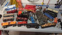 Photo of multiple Lionel train cars, S-2 Turbo Locomotive engine, Train Master controller, metal curved and straight tracks, water tower, and additional accessories on a white table.