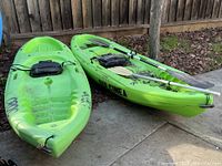 Two lime green Spitfire8 kayaks side by side on patio, paddles visible in one hull.