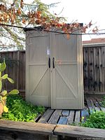 Front exterior view of tan Rubbermaid shed with two doors and black handles