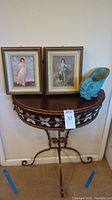 Photo showing demi-lune side table with floral inlay, two framed prints and metal nautilus shell bowl on top.