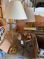Photo showing the brass swing arm floor lamp, Stiffel table lamp with shade, brass and red stone piano lamp on small round side table, and the metal base side table next to them.