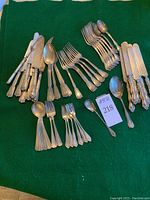 Wide assortment of forks, knives, spoons, serving pieces on green felt showing three distinct patterns