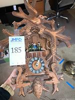 Full front view of cuckoo clock showing bird and branch carvings, dancing figures, clock face, and squirrels with pinecone weight.