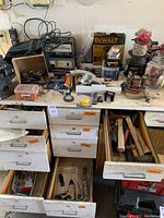 Workbench with Dewalt heat tool box, spools of wire, Schumacher and Mity Mite chargers, open drawers with hammers and hand tools